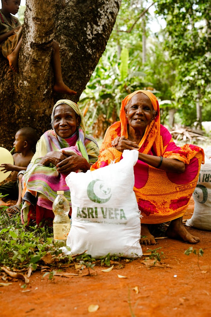 why-choose-us Two elderly women hold aid packages in a rural outdoor setting, sitting on red soil.